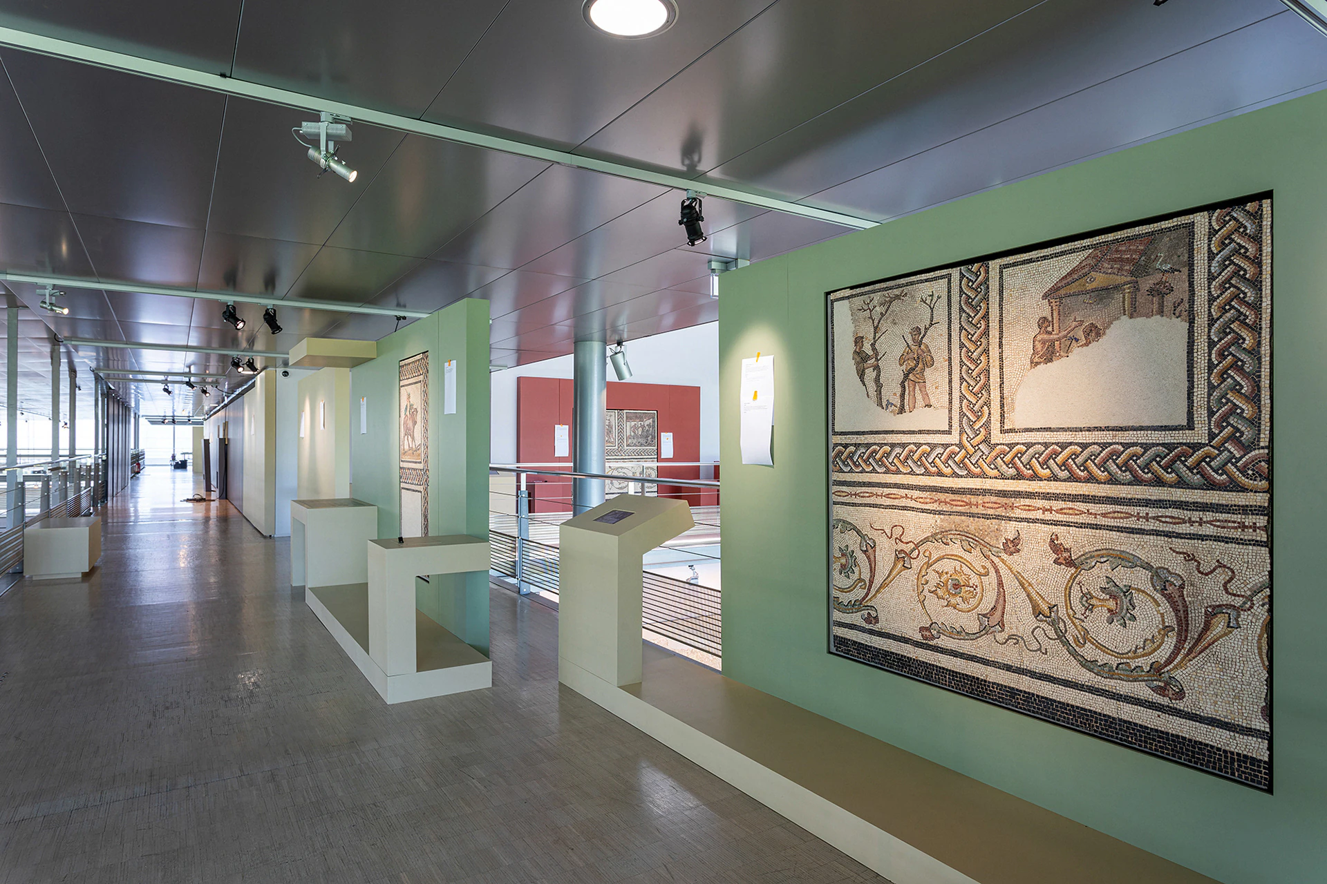 The exhibition: a Roman mosaic on a green wall, with display stands.