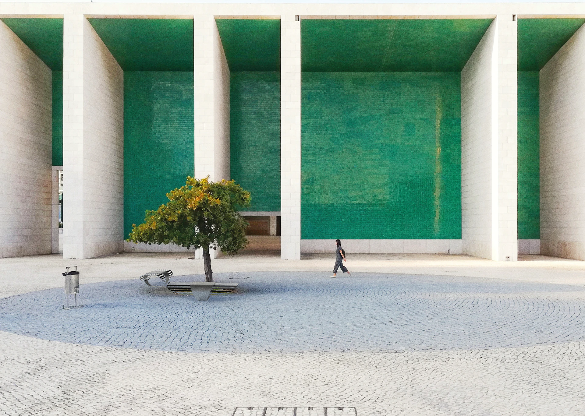 The bench in a stone square, beside a tree and a passer-by.